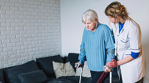 Carer helping older person on crutches